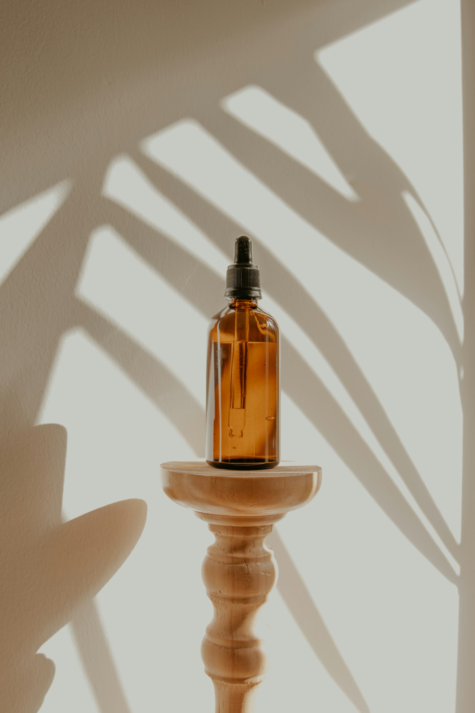 An amber flacon in soft palm-leaf shadow